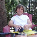 Anne Jarry assise dans sa cour avec sur les genoux sa raquette de tennis et des balles de Blind Tennis