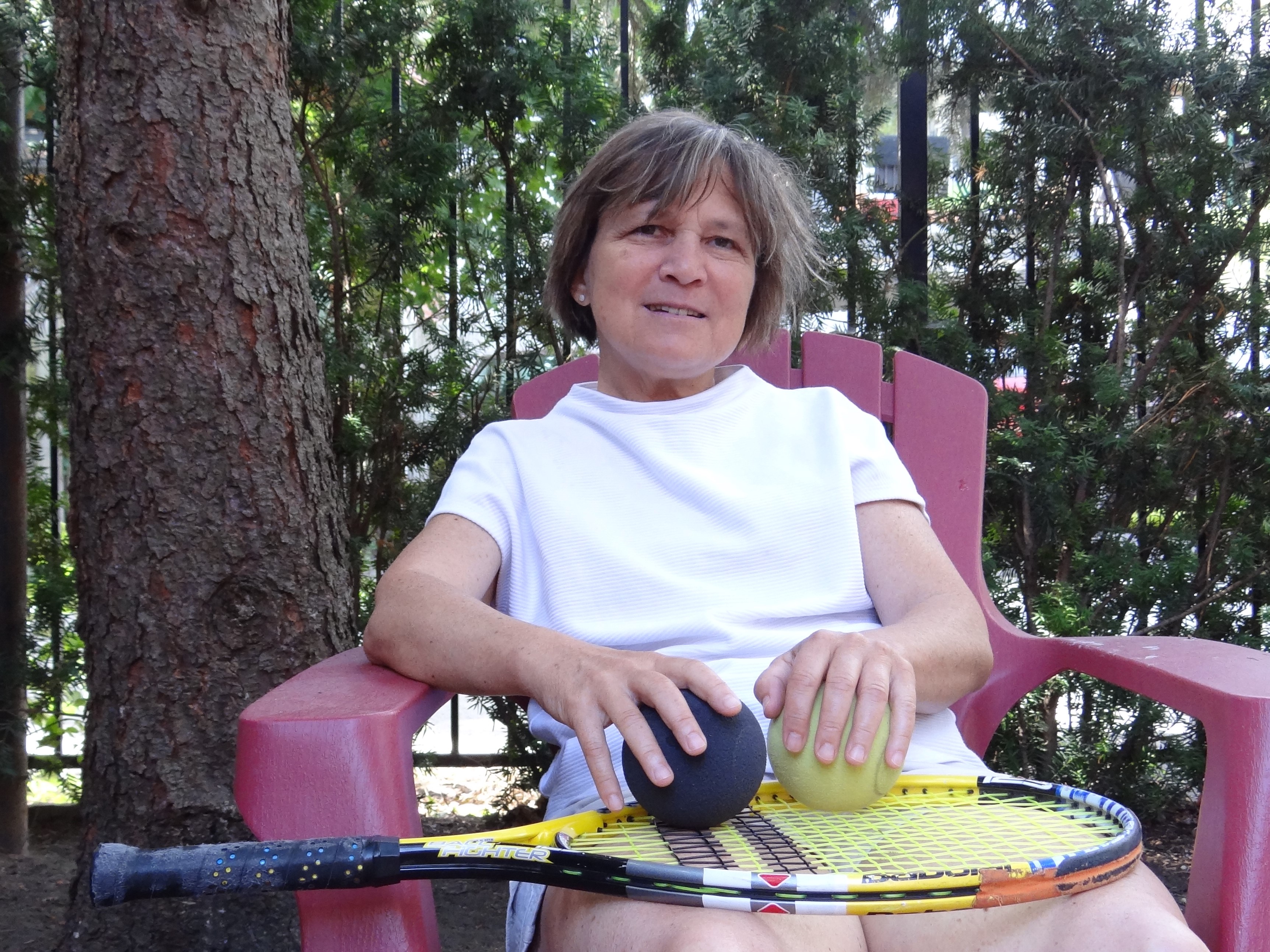 Anne Jarry assise dans sa cour avec sur les genoux sa raquette de tennis et des balles de Blind Tennis