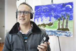 Florian Grond avec un casque d'écoute, devant la toile de Josée Boyer.