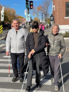 Mme Cathy Wong effectue une traversée de rue sous bandeau avec un bénévole et Yvon Provencher.