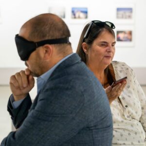 S. La Roche directeur du MAC et Martine Bedard, présidente du RAAMM, assis dos à dos dans une salle d'exposition. M. La Roche porte un bandeau opaque sur les yeux.