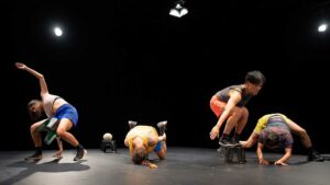 Quatre danseurs exécutent des mouvements de la chorégraphie Squat, sur scène.